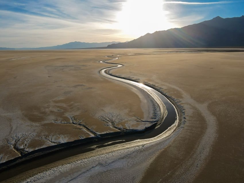 A thin winding river extends out to the distance surrounded by sandy unvegetated land