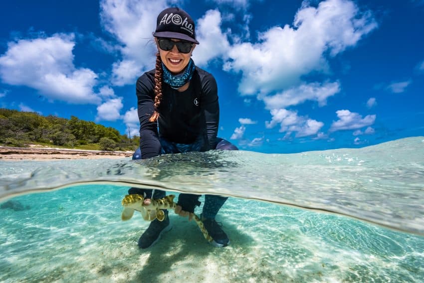 A woman kneels in the ocean and releases a small shark