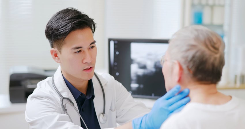 A doctor examines the throat of an elderly man for cancer
