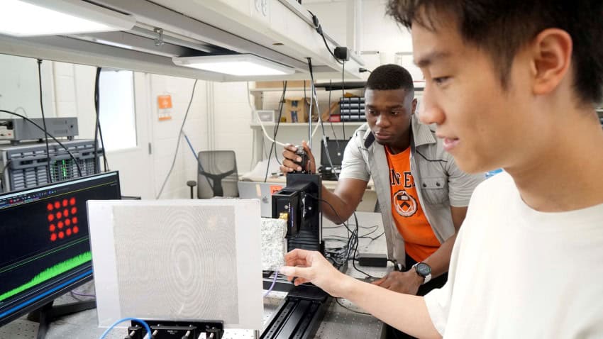 Two men stand in a physics laboratory setting up an experiment to send microwave airy beams around a barrier