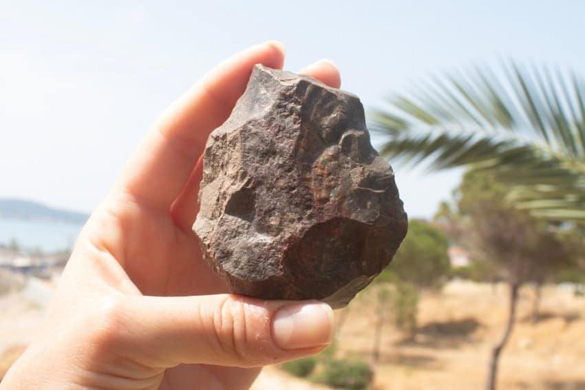 A hand holds up a rock which has been fashioned into an axe head-like shape