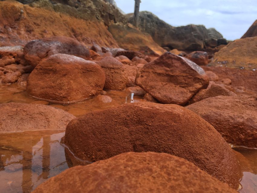 A close up picture of the sediment and rocks of one of five hot springs during low tide showing iron oxide mineral precipitates. Fatima li hau elsi 850