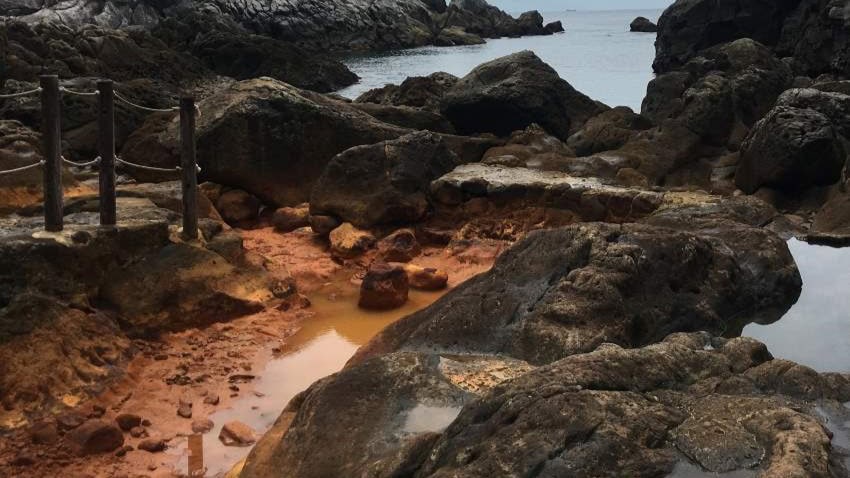A rust-coloured hotspring located next to the ocean