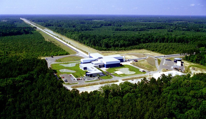 Facility in the middle of a lush green forest. L-shaped tubes protrude out into the distance to detect gravitational waves