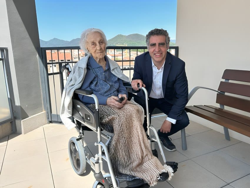 An elderly woman in a wheelchair photographed with a man in a suit on a balcony in spain