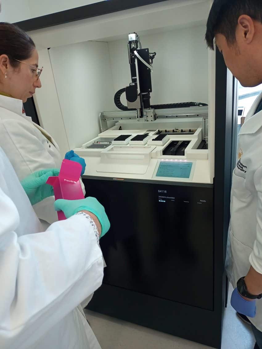 Researchers in lab coats surround a piece of technology encased in a black box