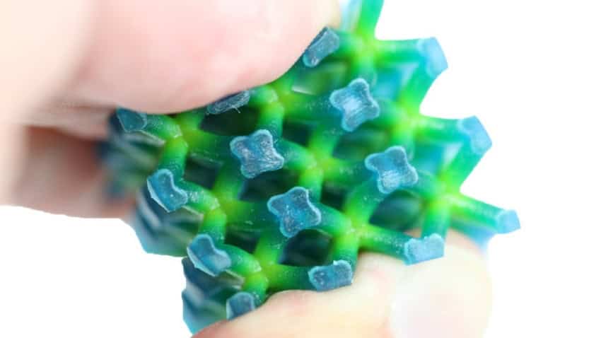 A cube-shaped lattice structure made out of green and blue materials which seamlessly transition from one colour to the other