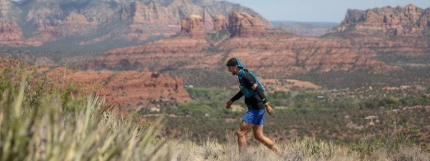 A man walks across an arid environment with stone monuments in the distance