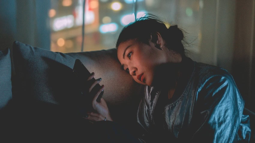 A young woman sits on her phone at night. She is looking concerned at the screen, potentially reading medical misinformation generated by llms