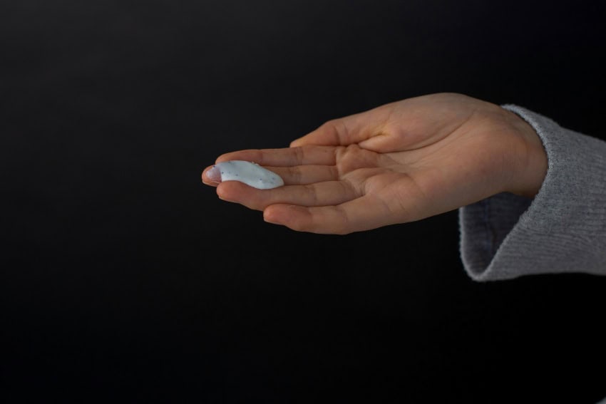 A hand holds white moisturiser against a black background