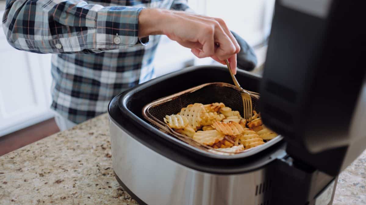 person cooking waffle fries in air fryer