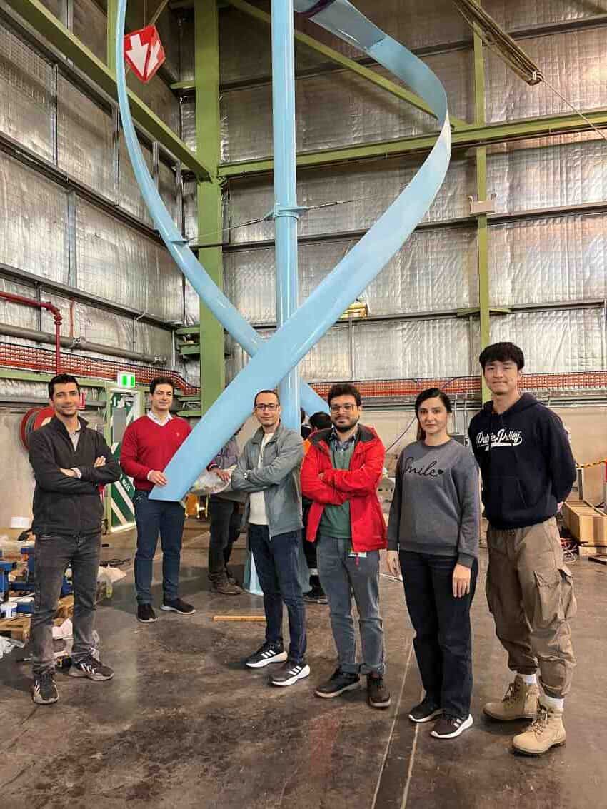 Group of people standing around vertical wind turbine