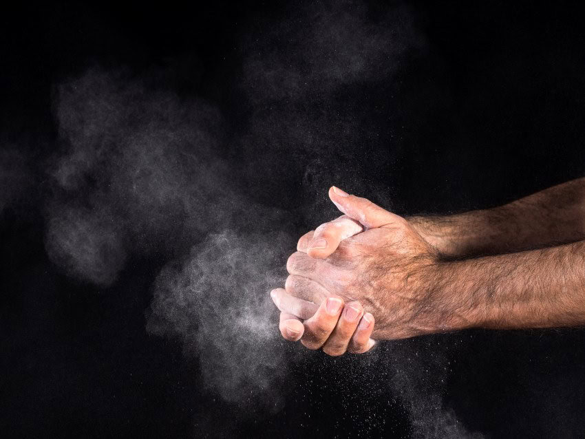 A man claps his hands, releasing white powder, against a black background