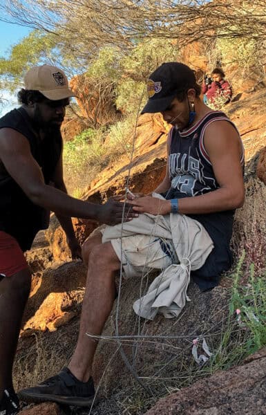 Two people holding a warru in a bag, giving an injection to the warru.