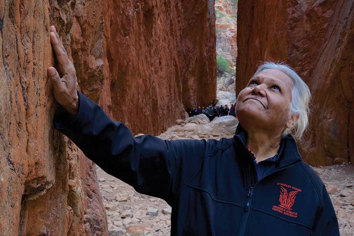 Older woman with grey hair gently touching the walls of a chasm.