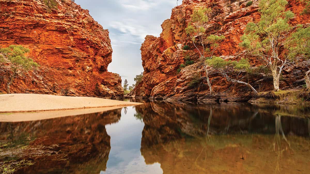 Red rock formations with a body of water in front.