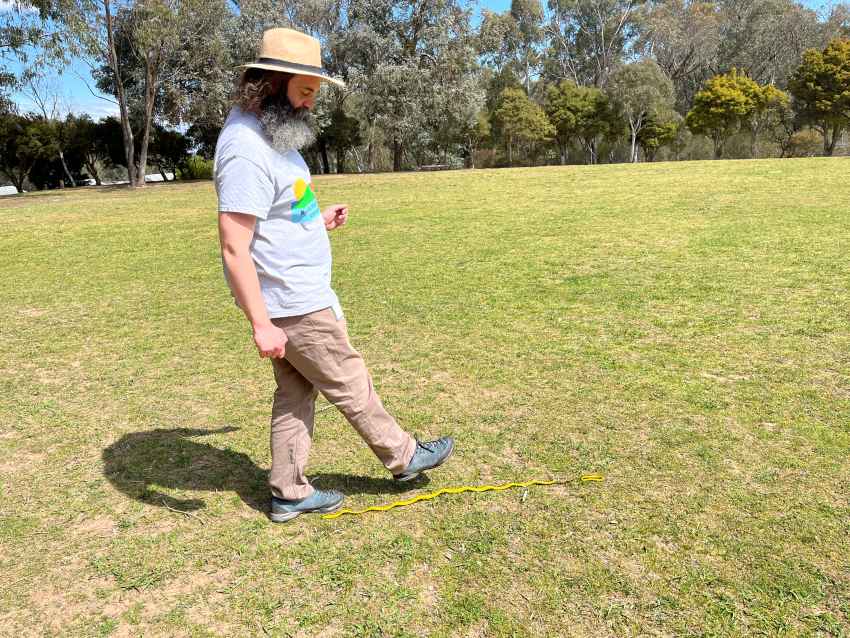 A man in a hat walks next to a tape measure, pacing out 1 metre.