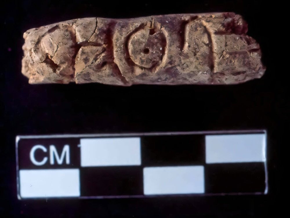 Ancient clay object with writing and cm scale on black background