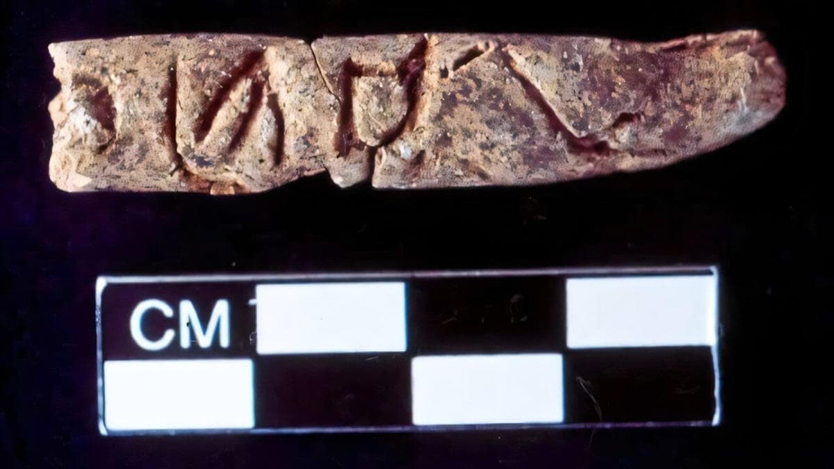 Ancient clay object with writing and cm scale on black background