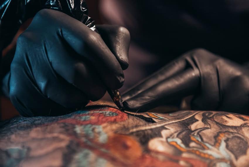 Black gloved hands tattooing skin becoming covered in colourful fresh tattoo.