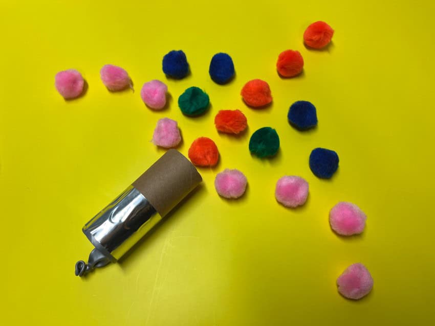 A pom pom cannon made of a toilet paper roll surrounded by pom poms in a geometric pattern. One of the activities for kids.