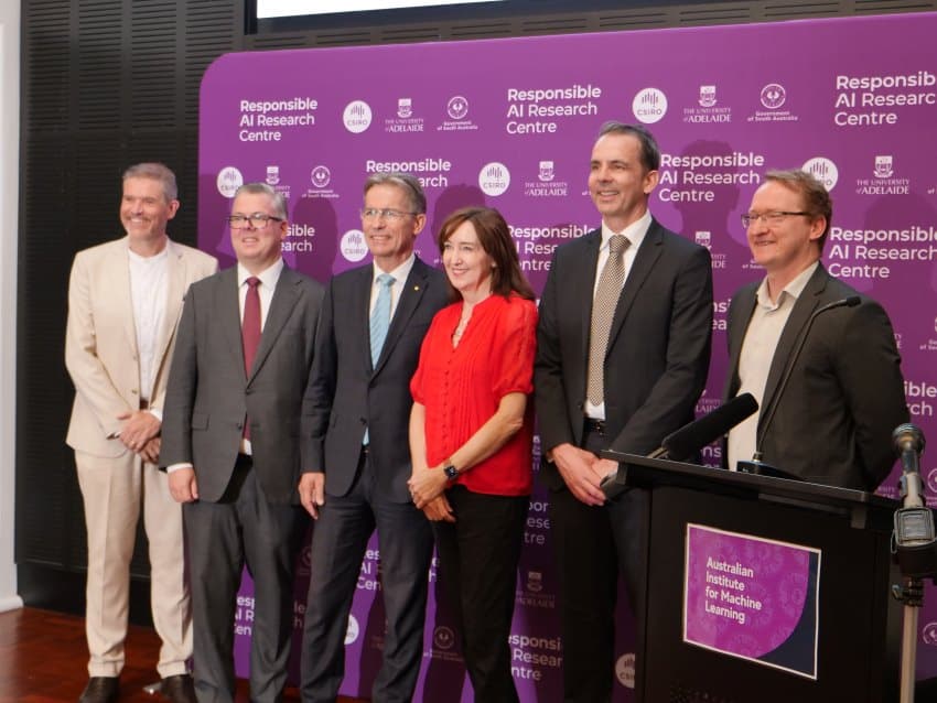 A photograph of 6 individuals standing in front of a purple backdrop with logos of the responsible ai research centre, csiro, the university of adelaide and the government of south australia