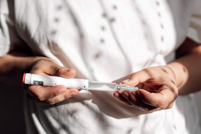 A person wearing a white t-shirt holds a semaglutide medication injector in front of themself.