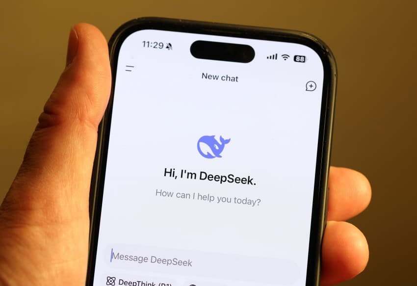 A hand holds a smartphone displaying the deepseek chatbot app, which reads: "hi, i'm deepseek. How can i help you today? "