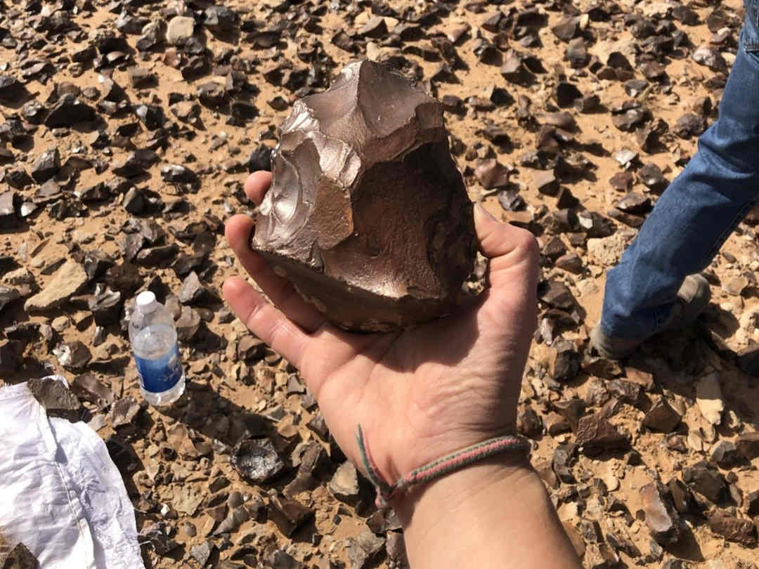 Hand holding ancient stone tool axe in desert