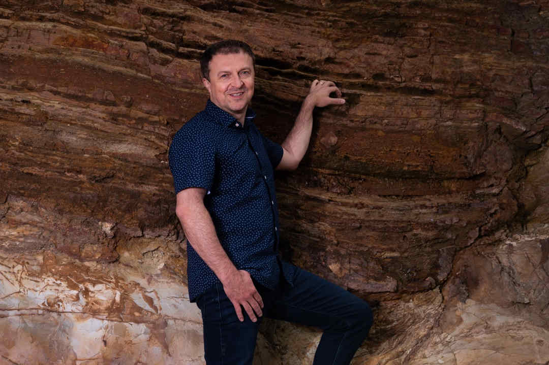 Geophysicist in blue shirt next to layers of rock