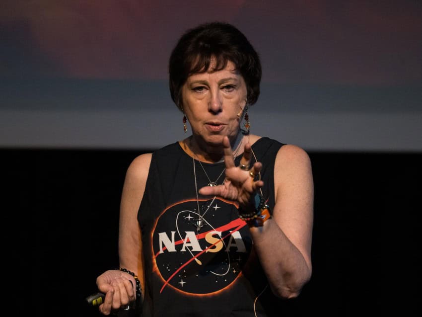 A woman wearing a nasa shirt speaks on a stage.