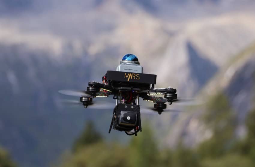 A small drone hovers with a mountainous scene in the background.