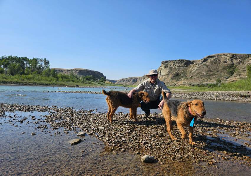 Two dogs with a man by a river, trained to haze grizzly bears.