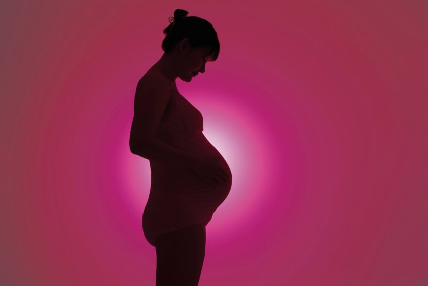 Silhouette of a pregnant person against a pink background with a bright light