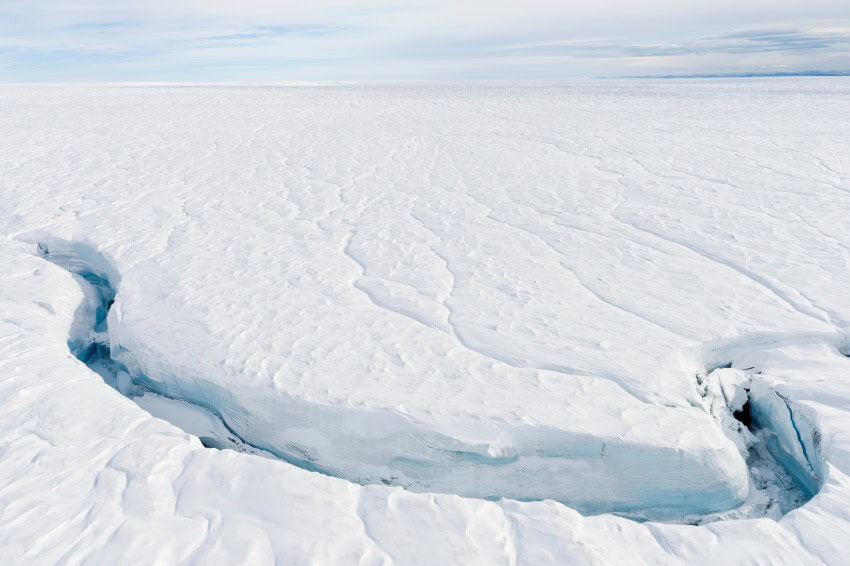 An expansive white ice sheet with a fracture in the foreground