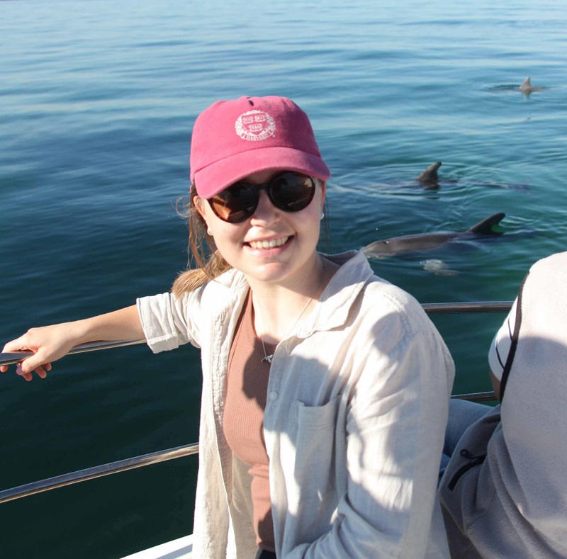 Female marine scientist wearing pink cap on boat with dolphins in background