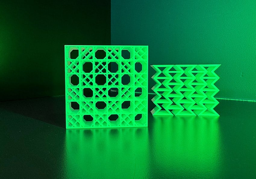 Two lattices are lit with a lime green light. The on on the left is made up of a square grid with diagonal struts. The one on the right is made of repeating hourglass shapes