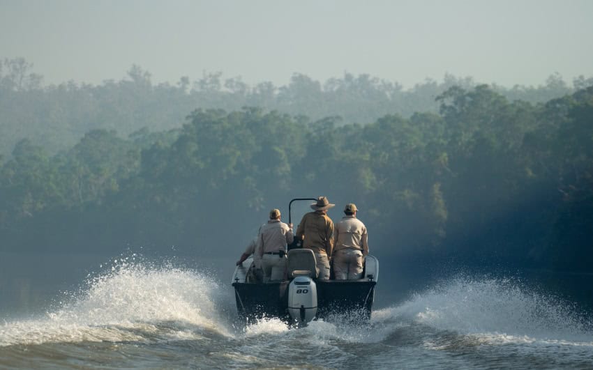 Several people dressed in khaki stand inside a boat speeding down a river