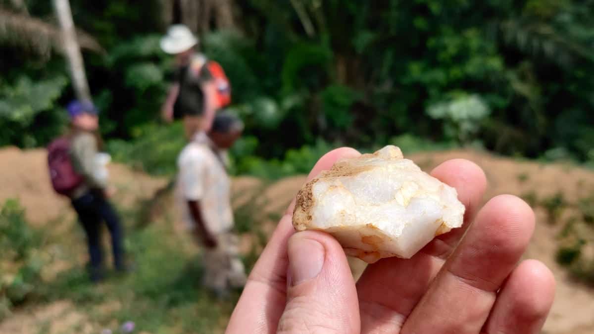 Hand holding ancient stone tool in forest with people in background