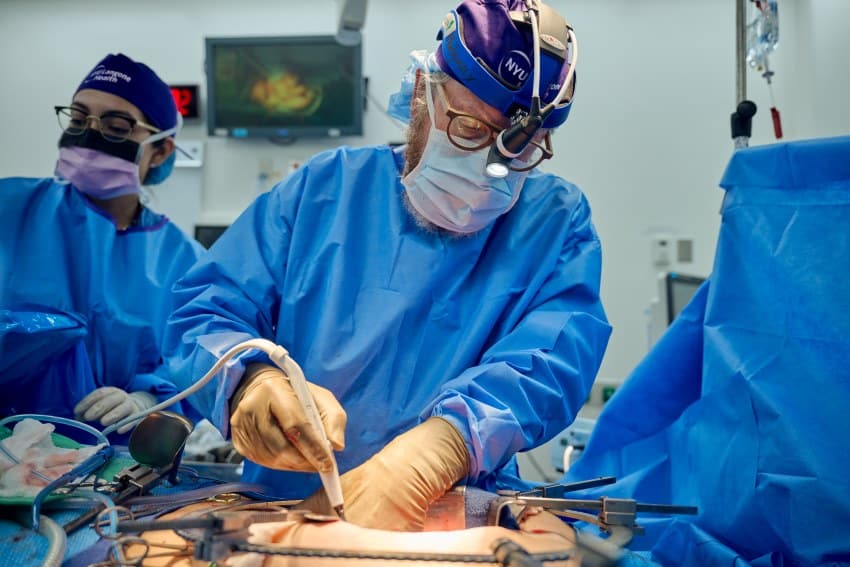 Surgeons in blue surgical gowns surround a patient whose abdomen has been opened up