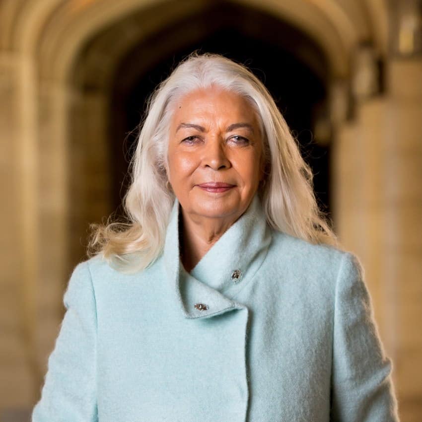 An older aboriginal woman with long white hear wears a pale blue coat