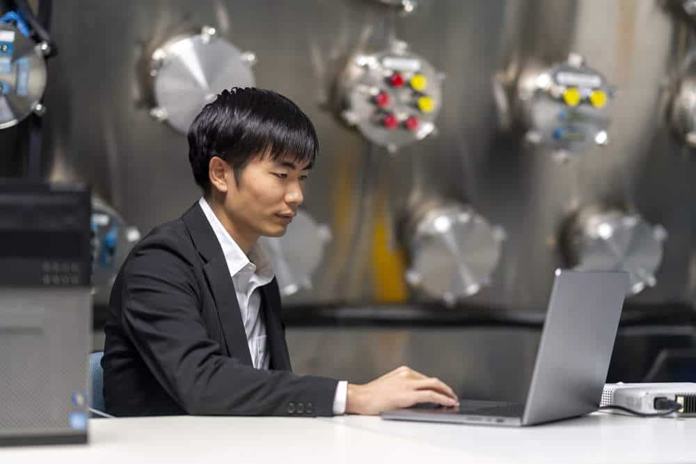 Man scientist sitting at desk with laptop in black blazer