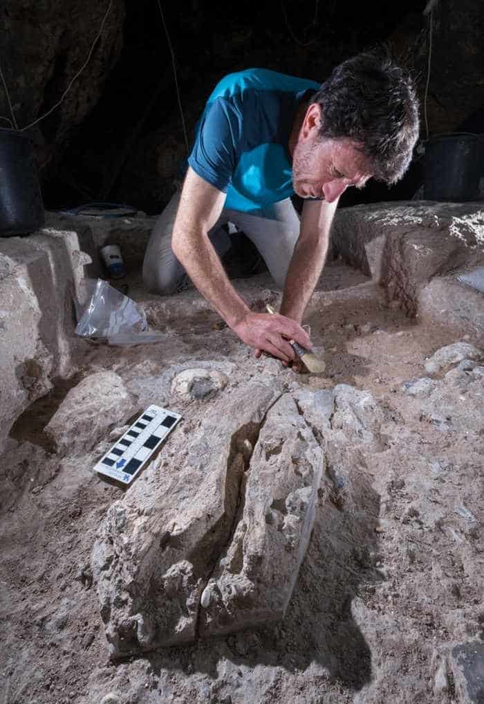 Man in blue t shirt excavating archaeological remains in cave with brush