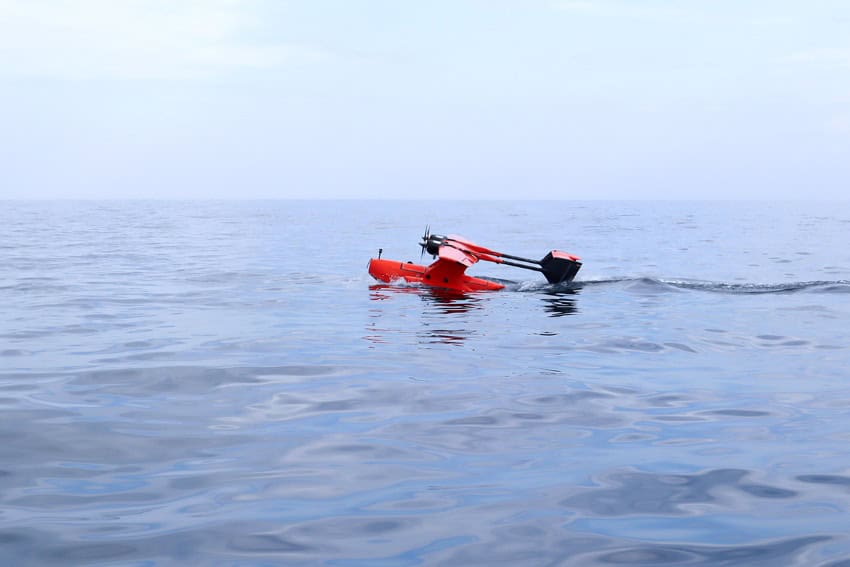 A small red drone in the shape of a sea plane gliding across the ocean's surface
