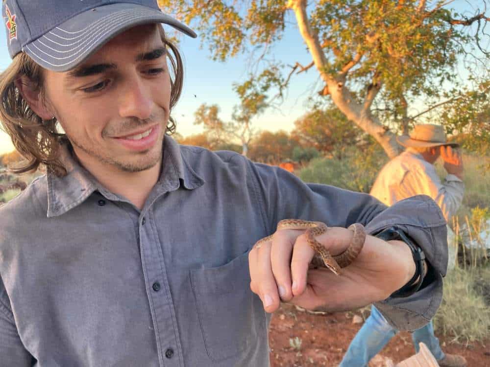 Australian bush researcher in cap with snake on hand