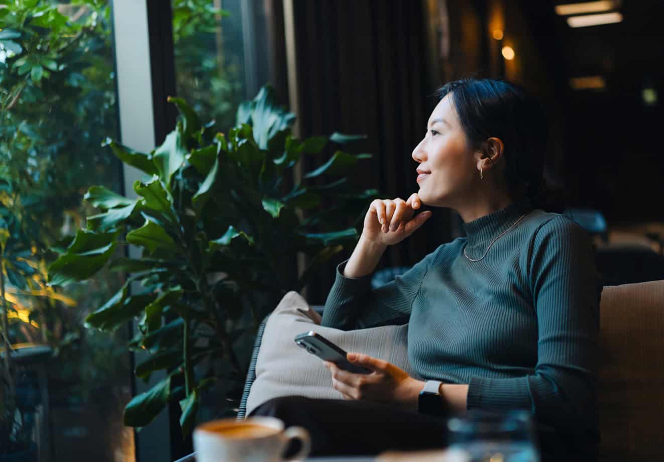 Inspired woman looking out window of a modern cafe while she holds her phone