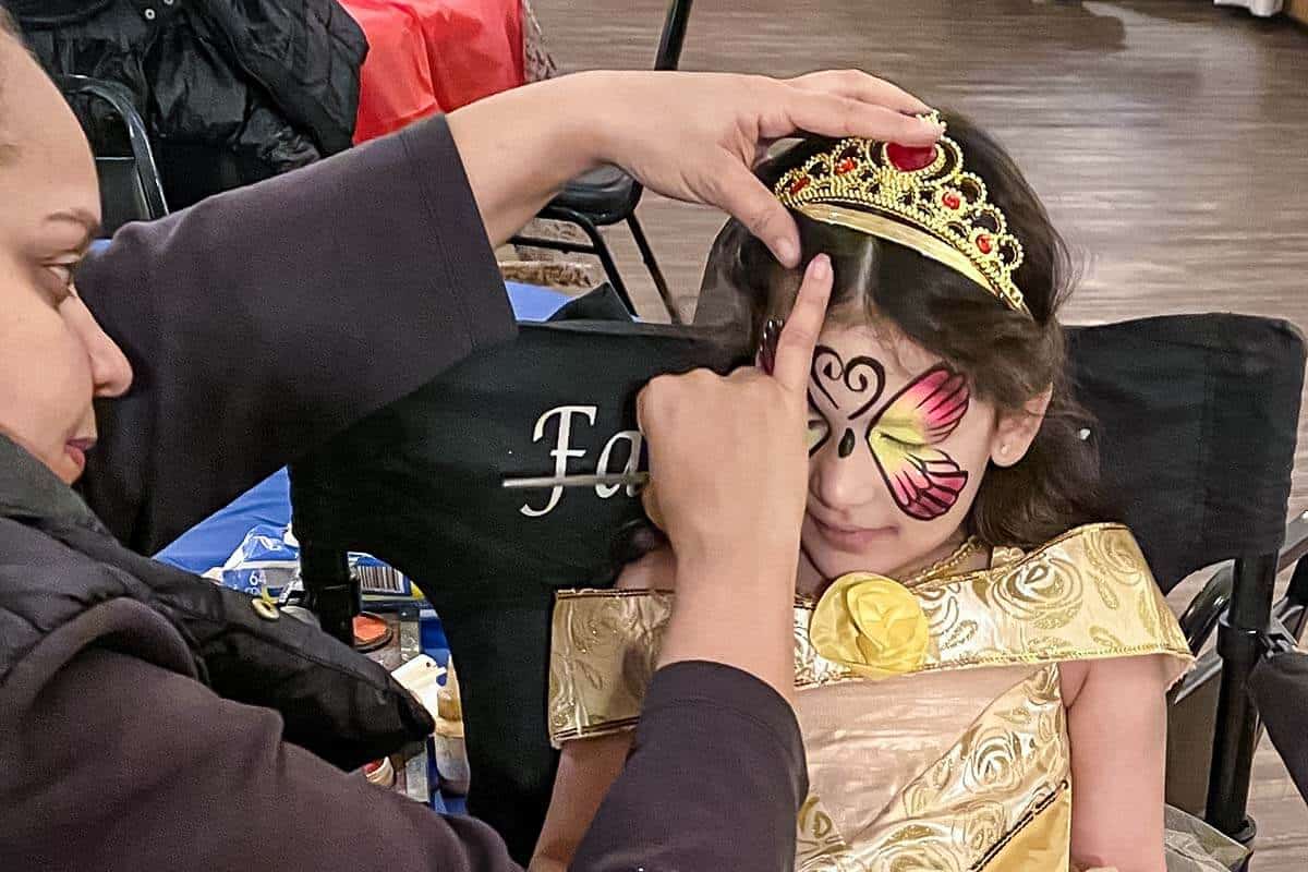 Face painter concentrates while applying face paint to a child who is wearing a princess outfit.