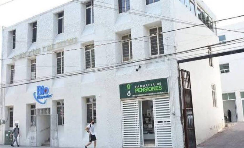 Farmacia de pensiones en Tlaxcala, fachada blanca de edificio con señalética verde y personas caminando en la calle.