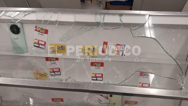 Vidrio roto en una exhibición de tienda con etiquetas de precios y un teléfono móvil.