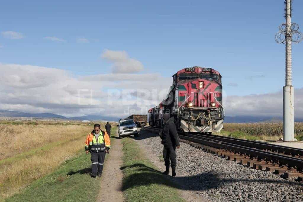 Vagones del tren en movimiento en medio de un campo, con personal de emergencia y un vehículo detenido cerca de las vías, bajo un cielo parcialmente nublado en Tlaxcala, México.